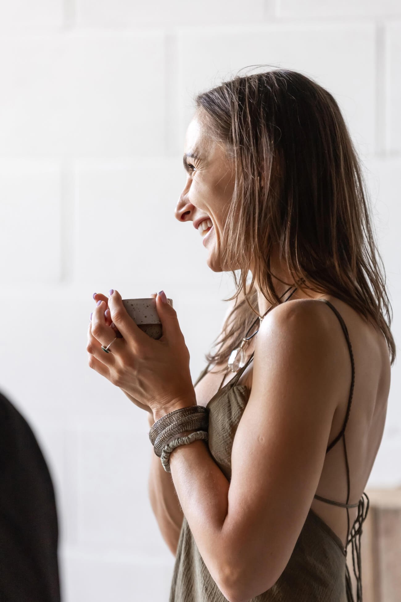 A woman with brown hair holding a cup with ceremonial cacao and smiling in a well-lit indoor setting.