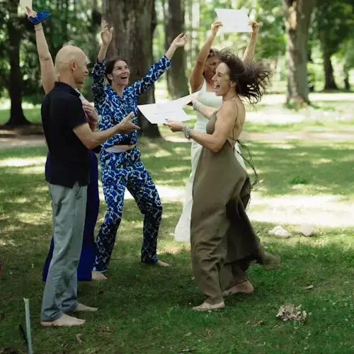 A cheerful group of five women and one man outdoors in a nature, celebrating and holding certificates, with some raising their hands and smiling.