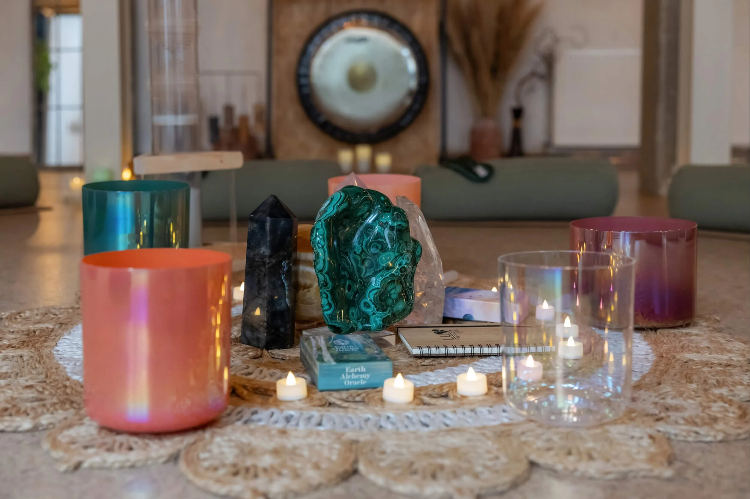 A table setup for a spiritual or meditation session with candles, colourful crystals, oracle cards, and a small notebook, in a cosy indoor space.