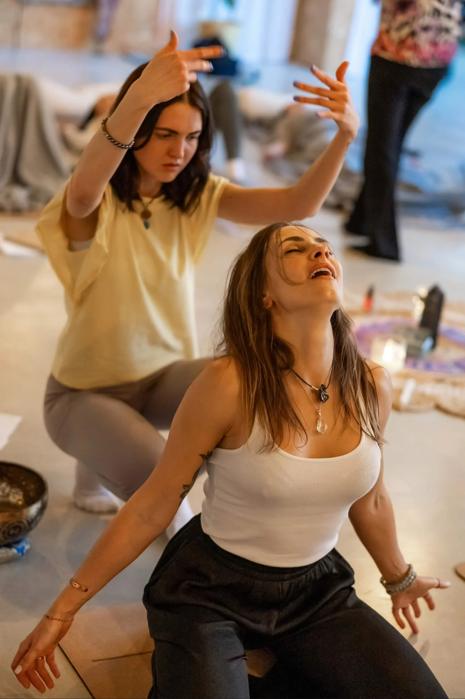 Two women in activation with peaceful faces and energy being present in a room, other people are behind them in activation process