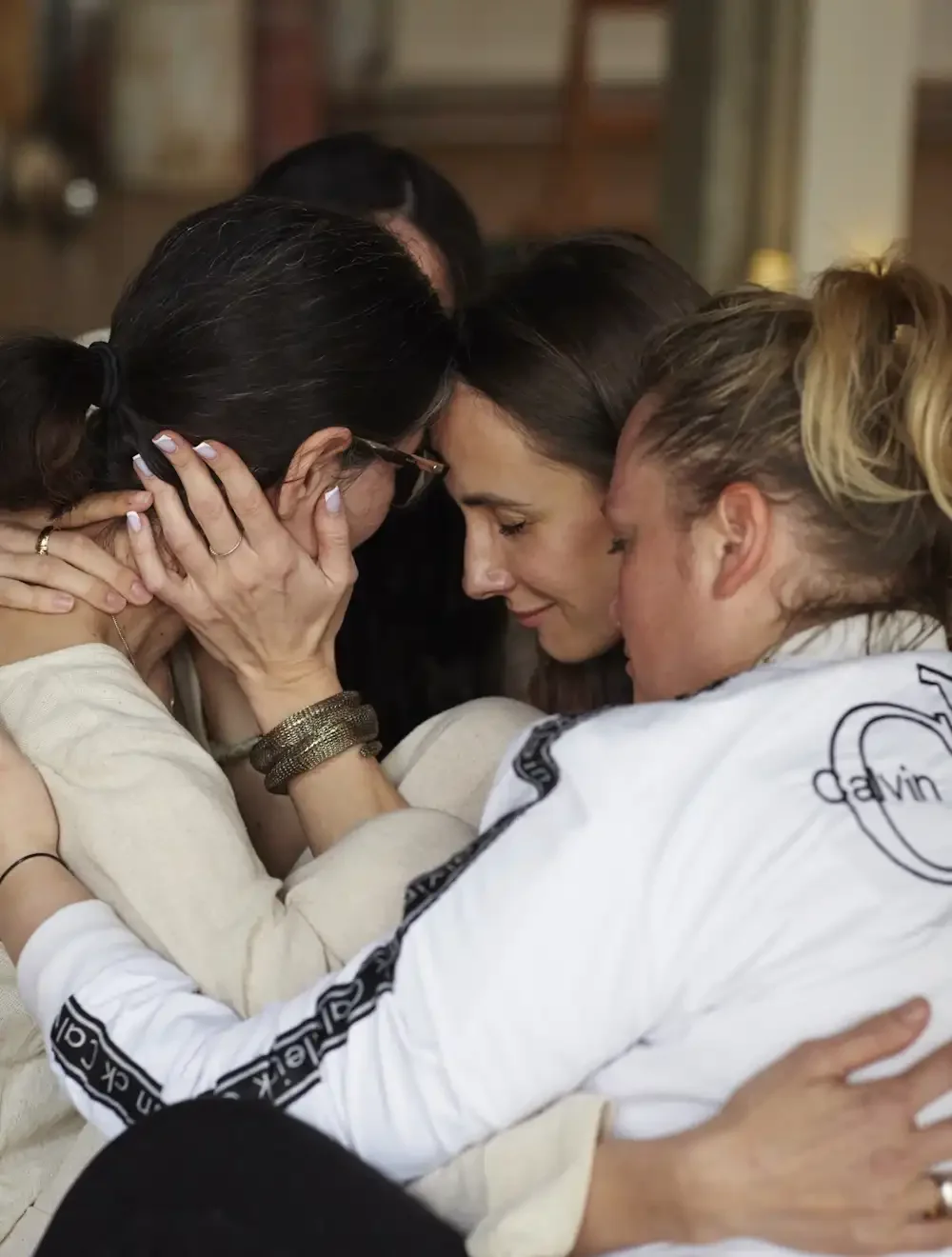Four women are hugging each other in a loving and uniting moment and one is holding a face of another woman