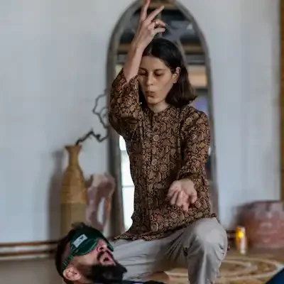 A woman is guiding a session with hands in mudra, energy present and a man on the floor being activated in energy flow.