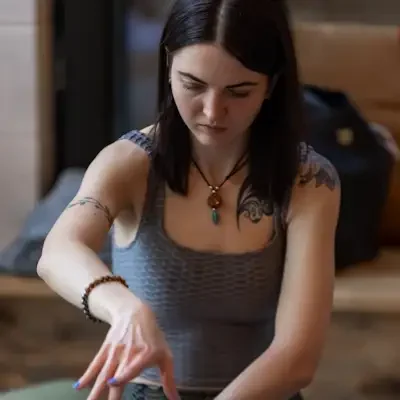 A woman with dark hair, tattoos, and jewellery is practicing Kundalini Activation on a person lying down.