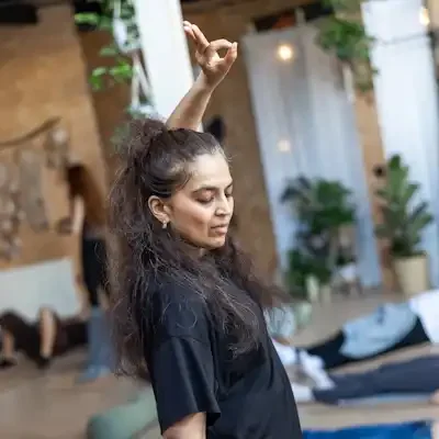 A woman standing doing mudra with her hands and people are on the floor peacefully resting.