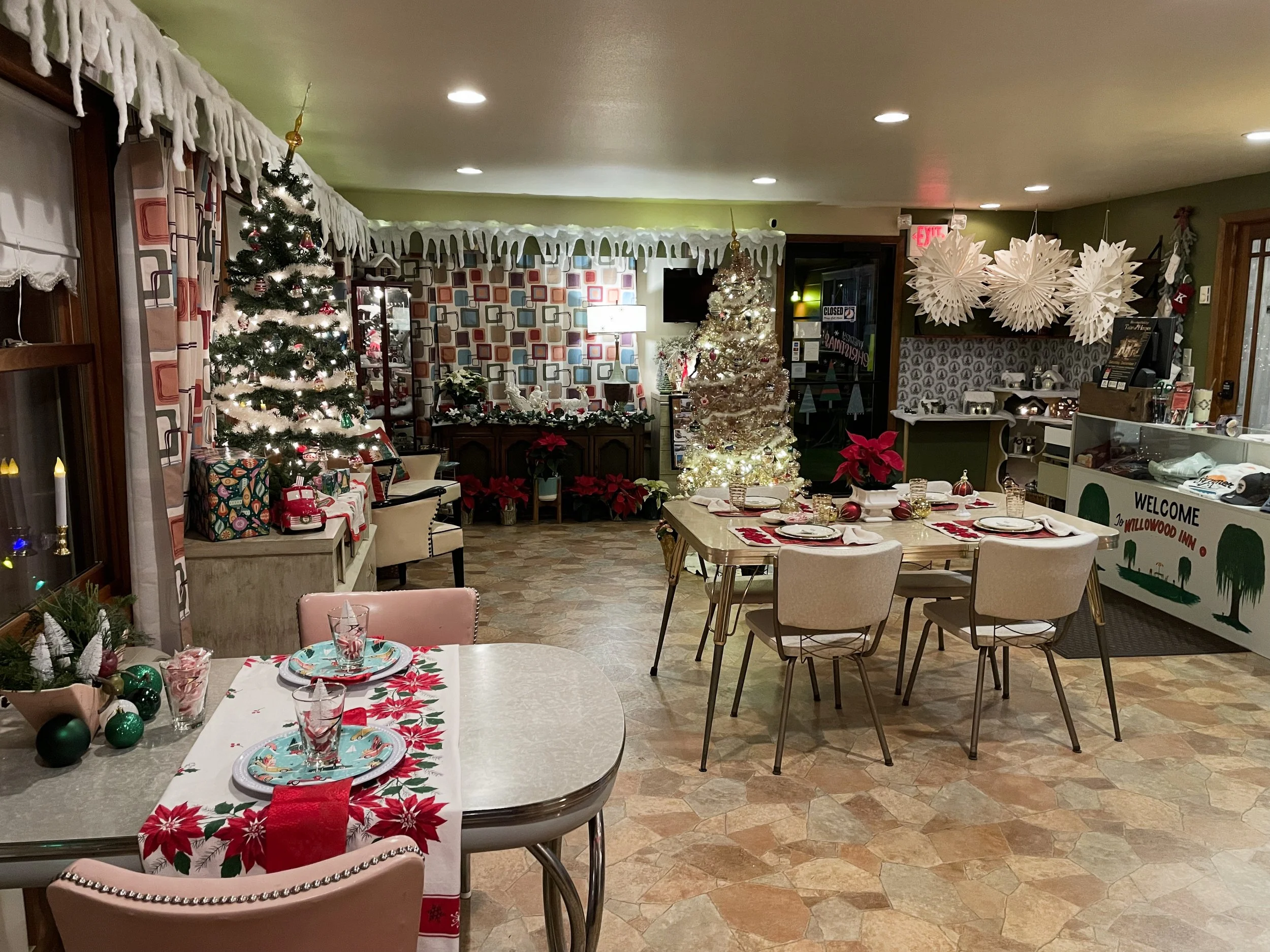 A festive Christmas interior with decorated trees, poinsettias, table settings, and holiday decorations.