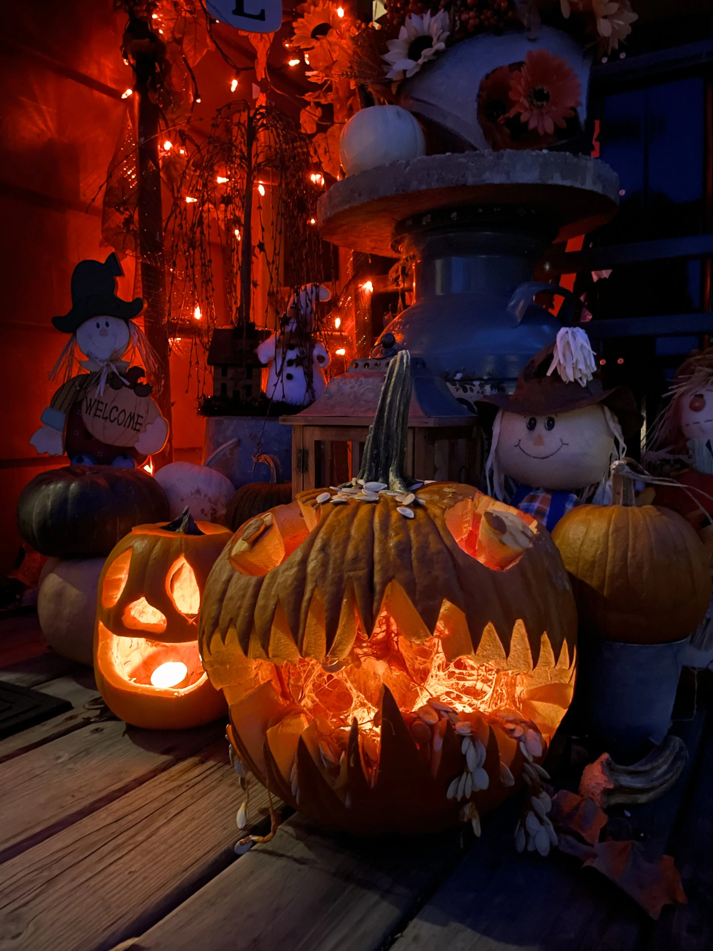 A glowing Halloween pumpkin with a carved face, surrounded by other pumpkins and Halloween decorations, illuminated with orange lights.