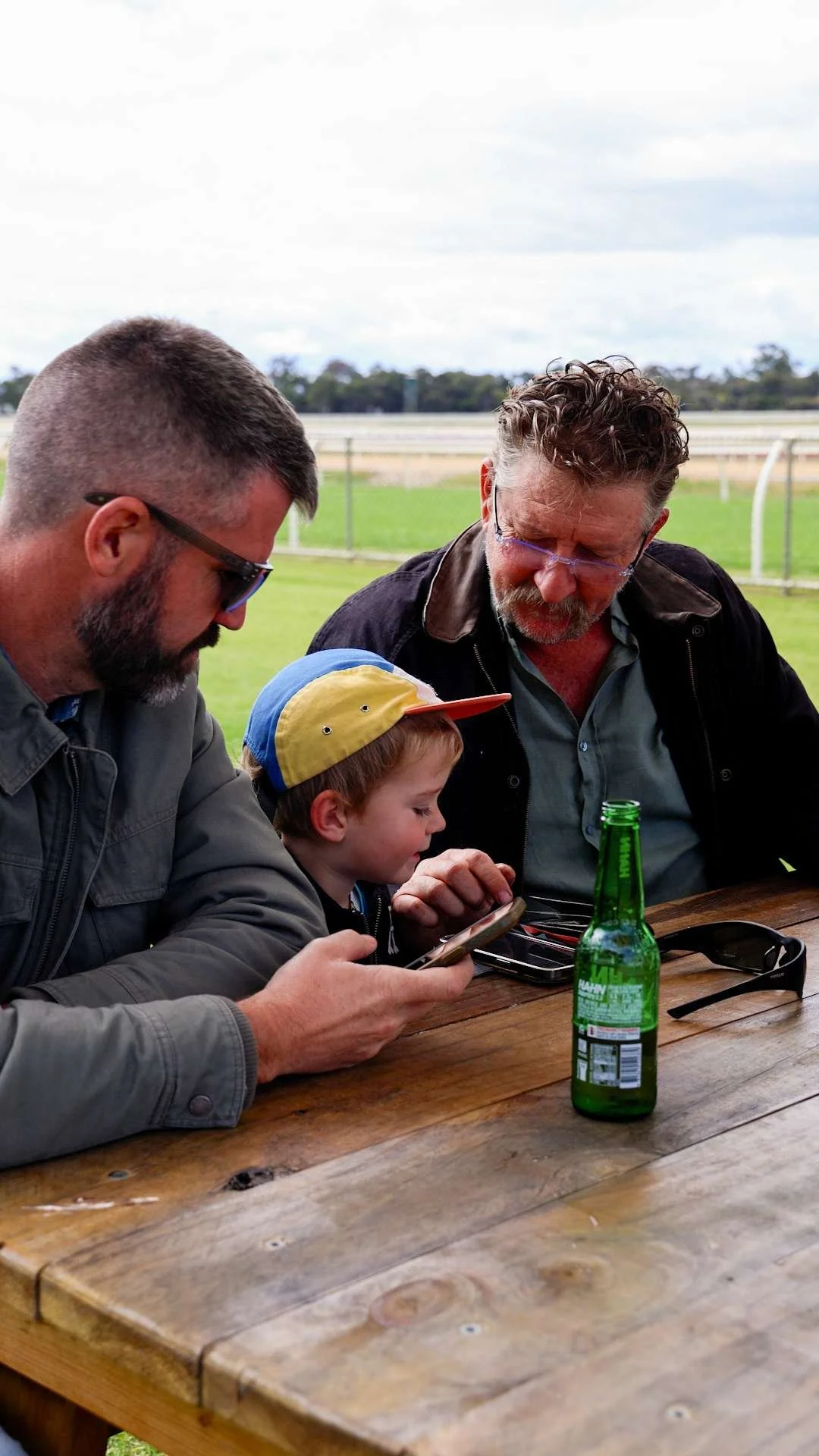 Three people, two adult men and a young boy, sitting at a wooden table at Bunbury Turf Club Family Fun Day.