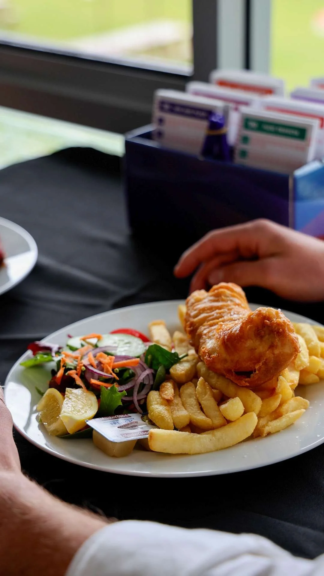 Plate of fish and chips with side salad in front of a window.
