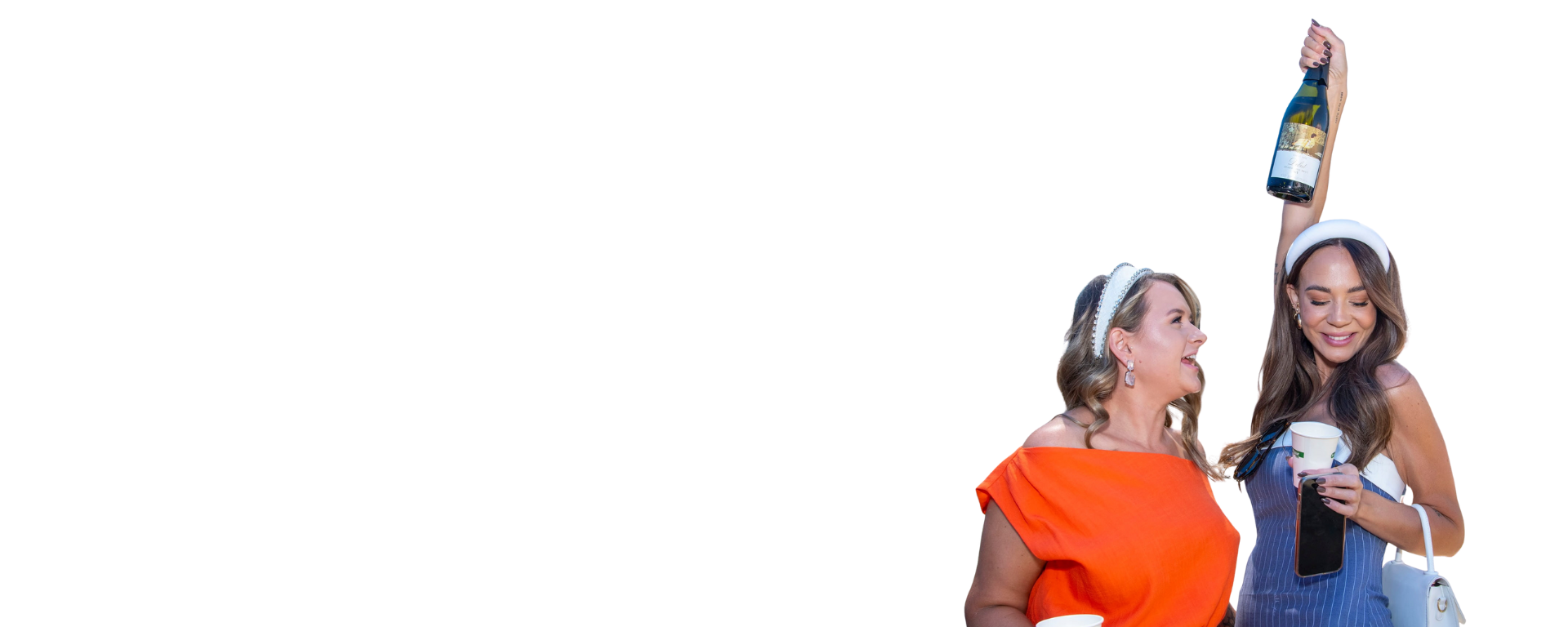 Two women celebrating together, one holding a bottle of wine and the other holding a cup and phone, smiling and enjoying the moment.