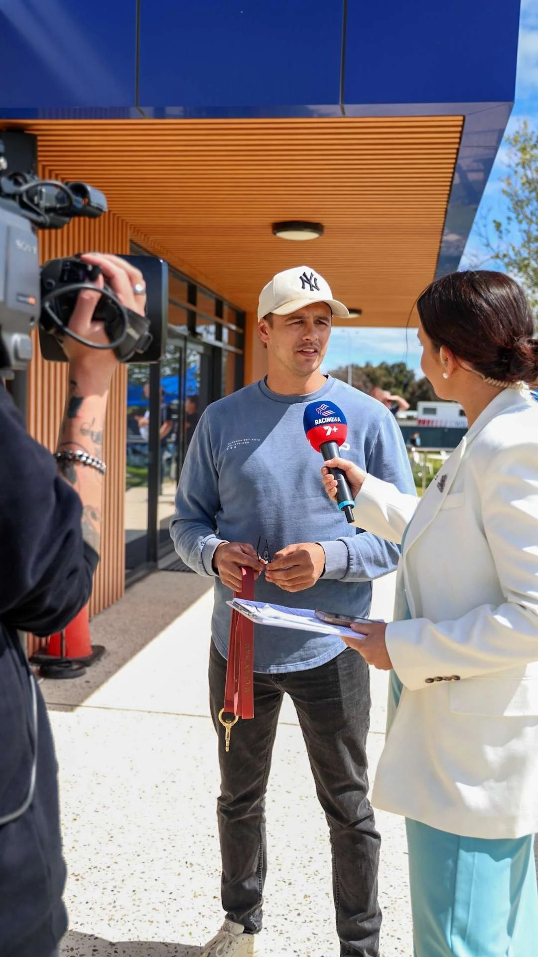 A man is being interviewed by a woman with a microphone outside Bunbury Turf Club.