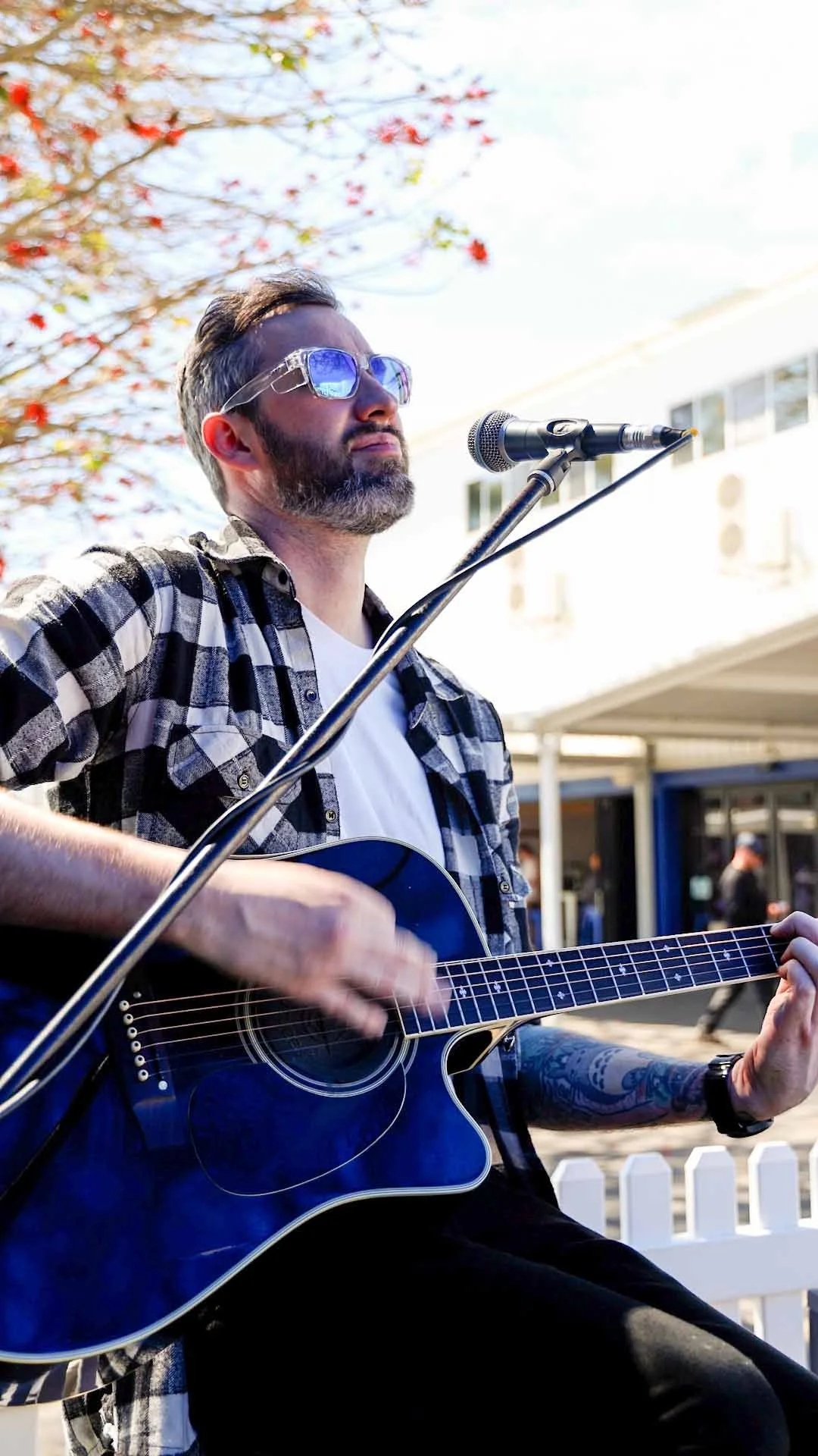 A man with a beard and sunglasses playing an acoustic guitar outdoors at Bunbury Turf Club Family Fun Day.