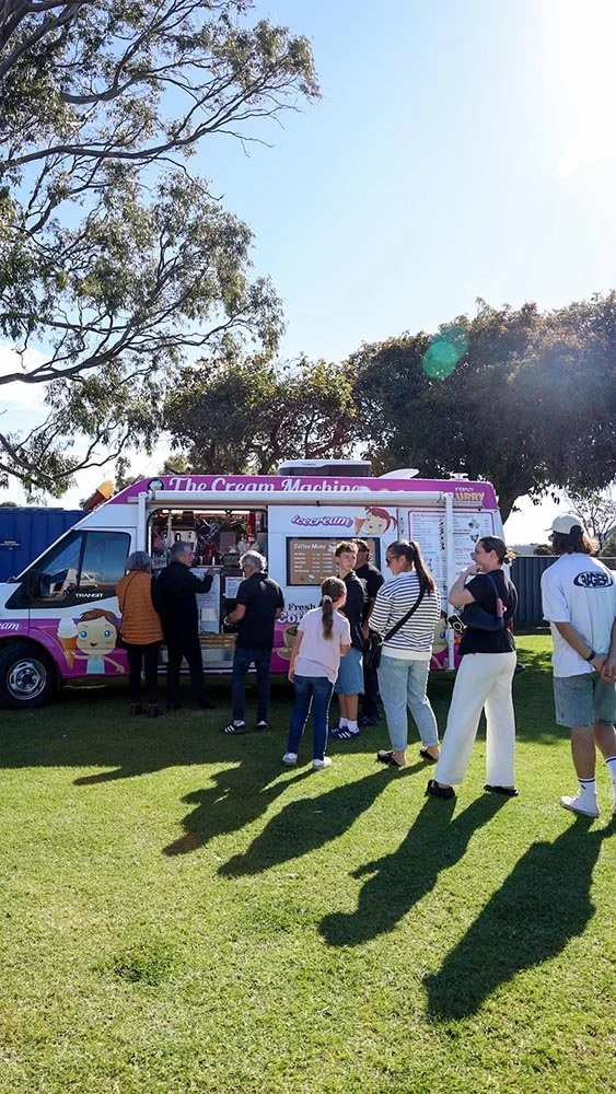 People standing in line at a pink and white ice cream truck with trees and a clear blue sky in the background at Bunbury Turf Club Family Fun Day.
