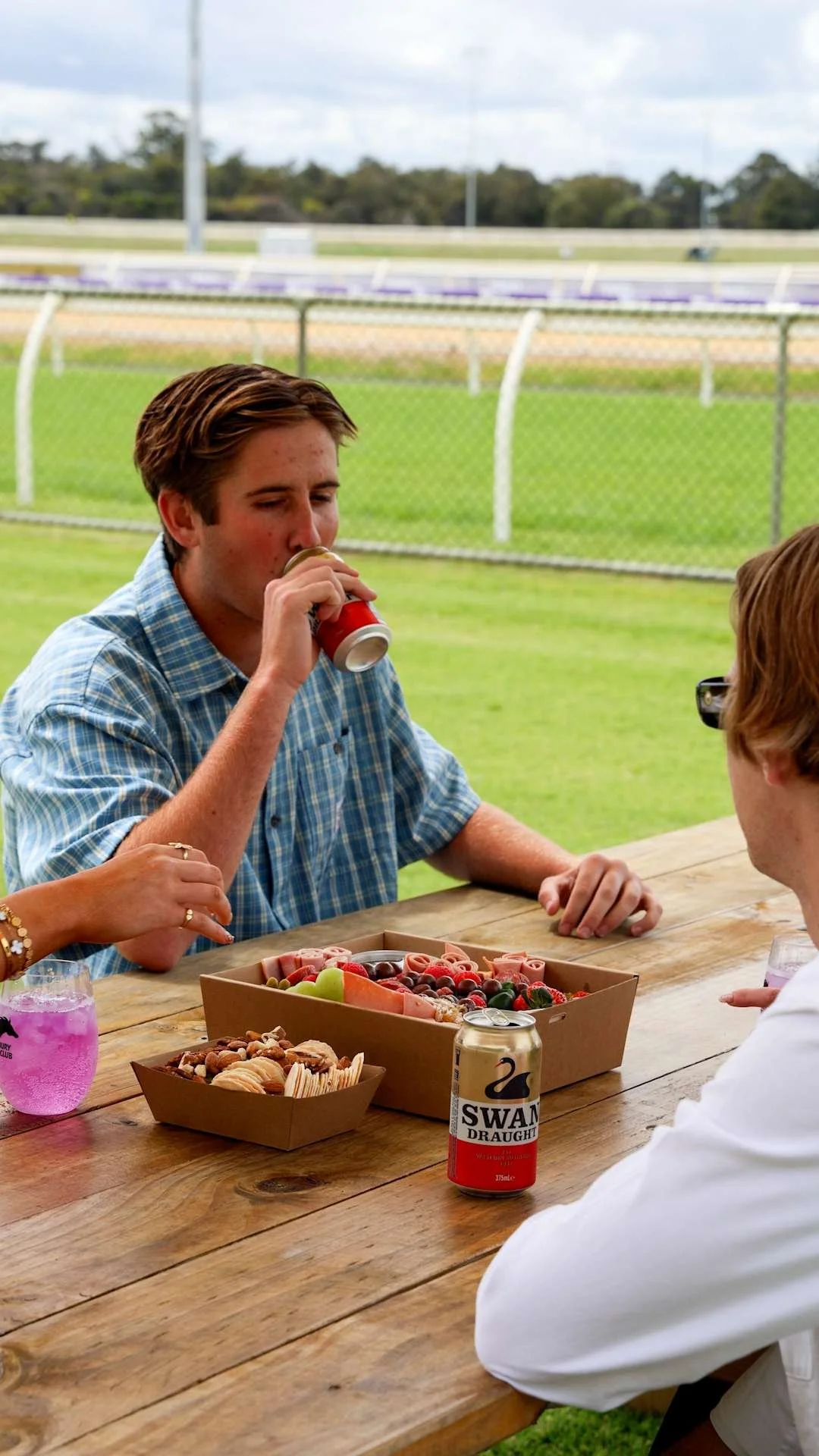 People sitting at a wooden table outdoors, enjoying snacks and drinks at Bunbury Turf Club Family Fun Day.