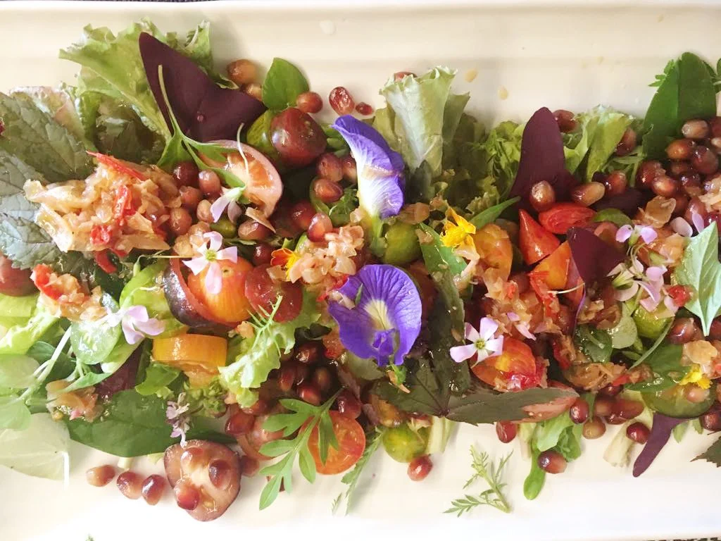 A colorful mixed salad with various greens, cherry tomatoes, edible flowers, and berries.