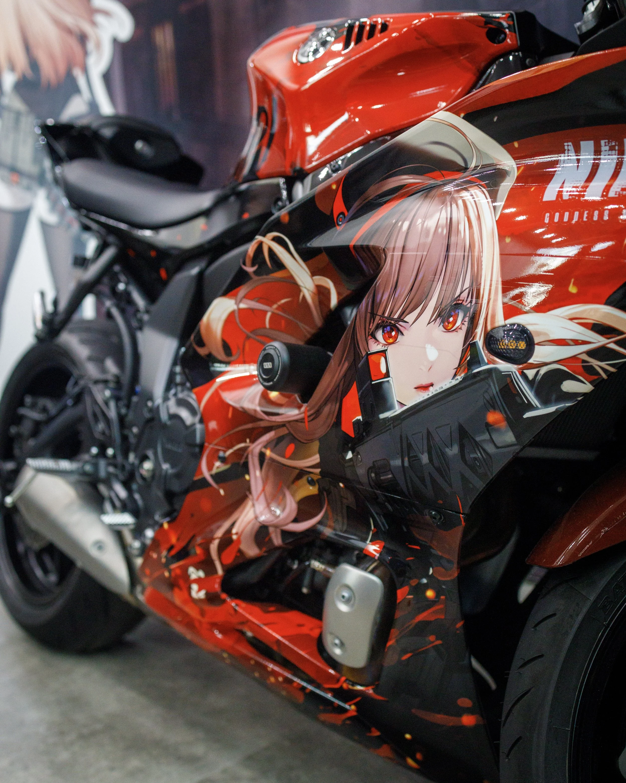 A close-up of a motorcycle featuring anime-style artwork of a girl with long brown hair and red eyes, with red, black, and beige colors.