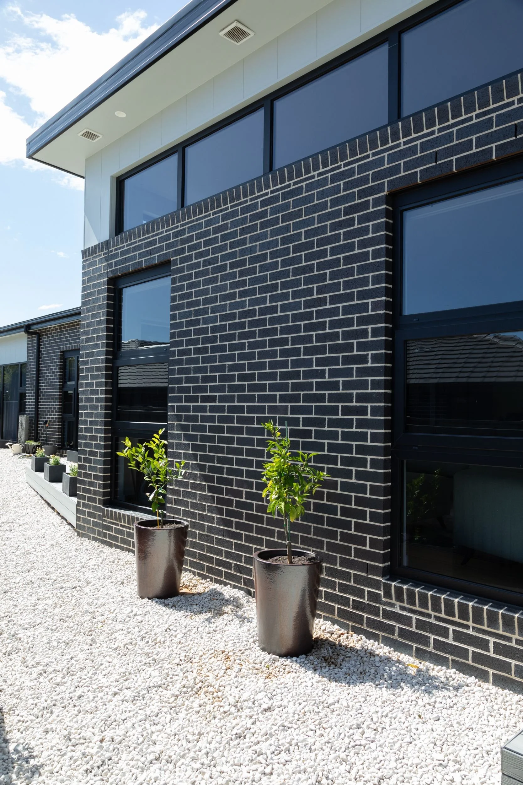 Modern architecturally designed house with black brick exterior, large uPVC framed double glazed Windows and clean landscaping in the foreground.