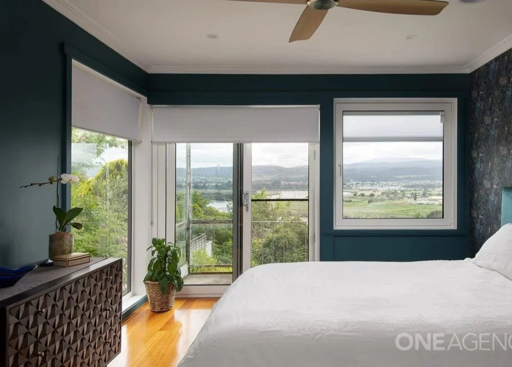 A renovated bedroom with a large bed, new curtains, black-out blinds, dark paint washed walls, plants and greenery, natural living, sustainable modern living.