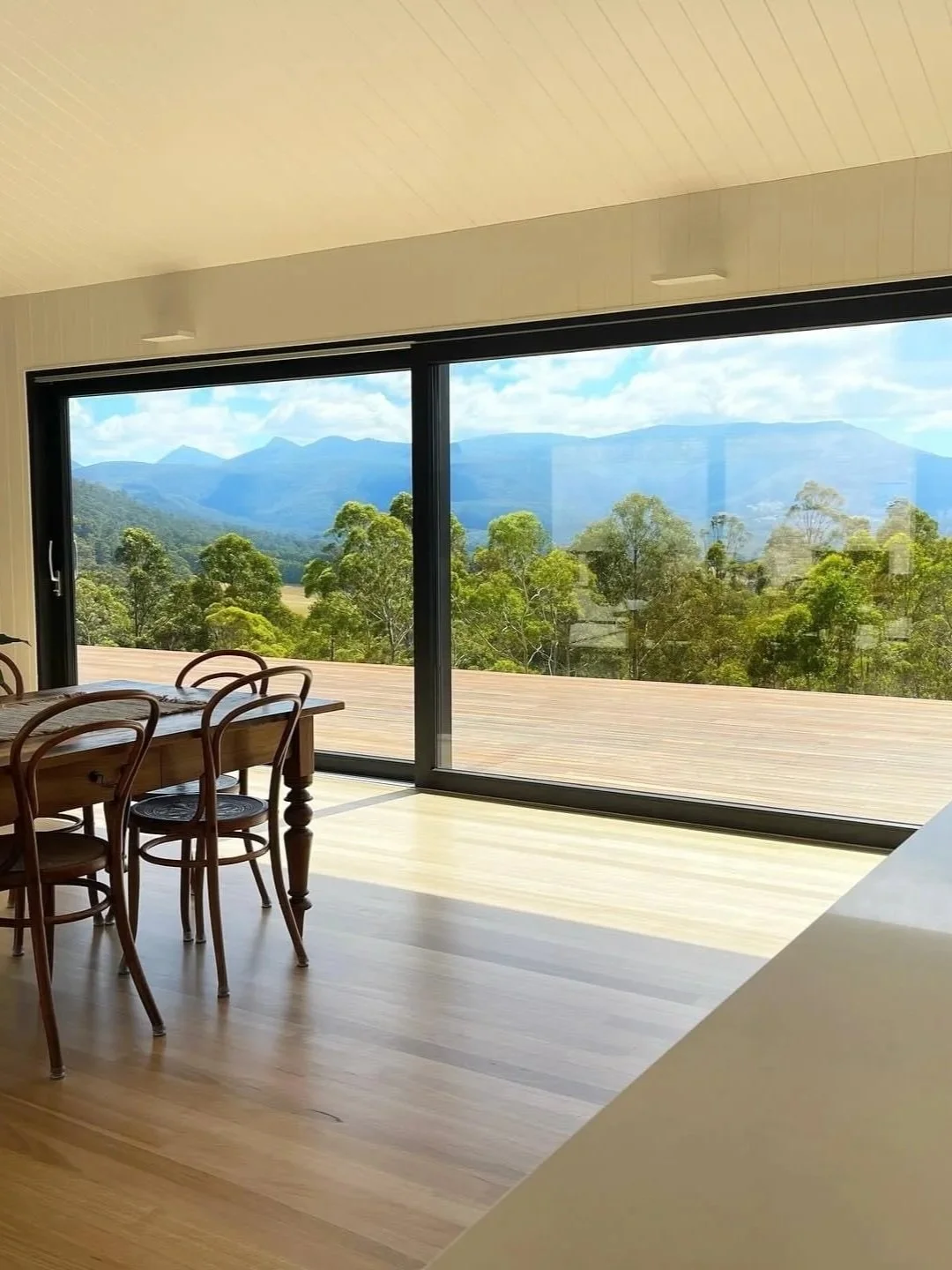 Rural living with a magnificent view of the Victorian alps or hinterlands which is seen through large Lift and Slide sliding glass doors which opens out to a deck and a scenic mountain view with trees and blue sky.