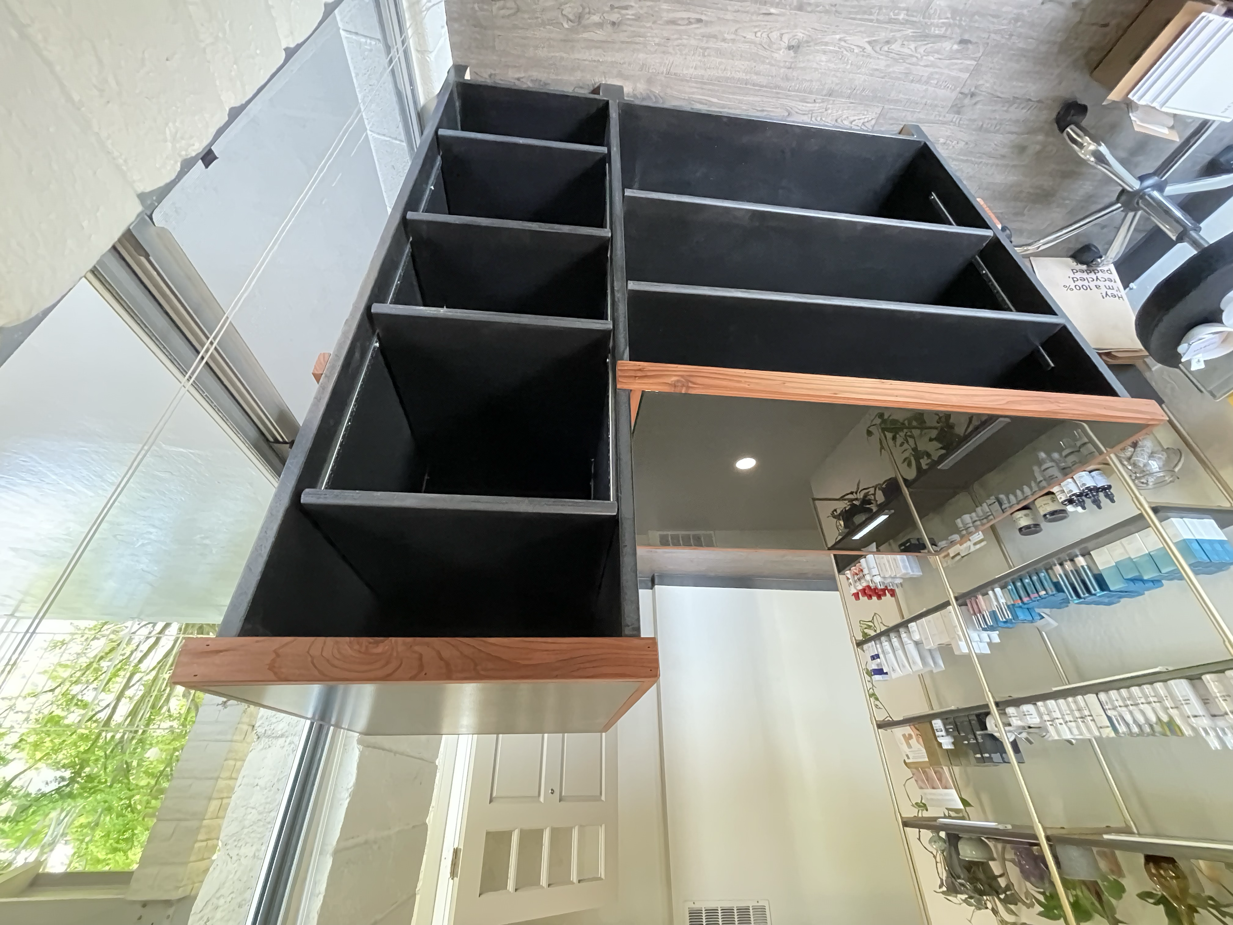 A black wooden display unit with multiple compartments next to a glass mirror, inside a retail or pharmacy store.
