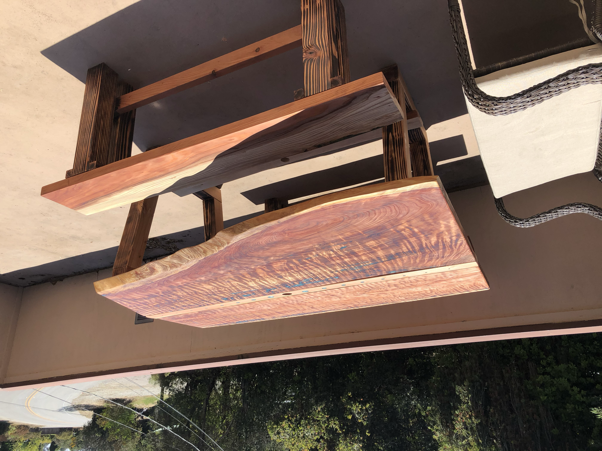 Two polished wooden slabs with natural edges, placed on a patio, casting shadows. One slab is reddish with prominent grain, the other darker with a smooth surface.