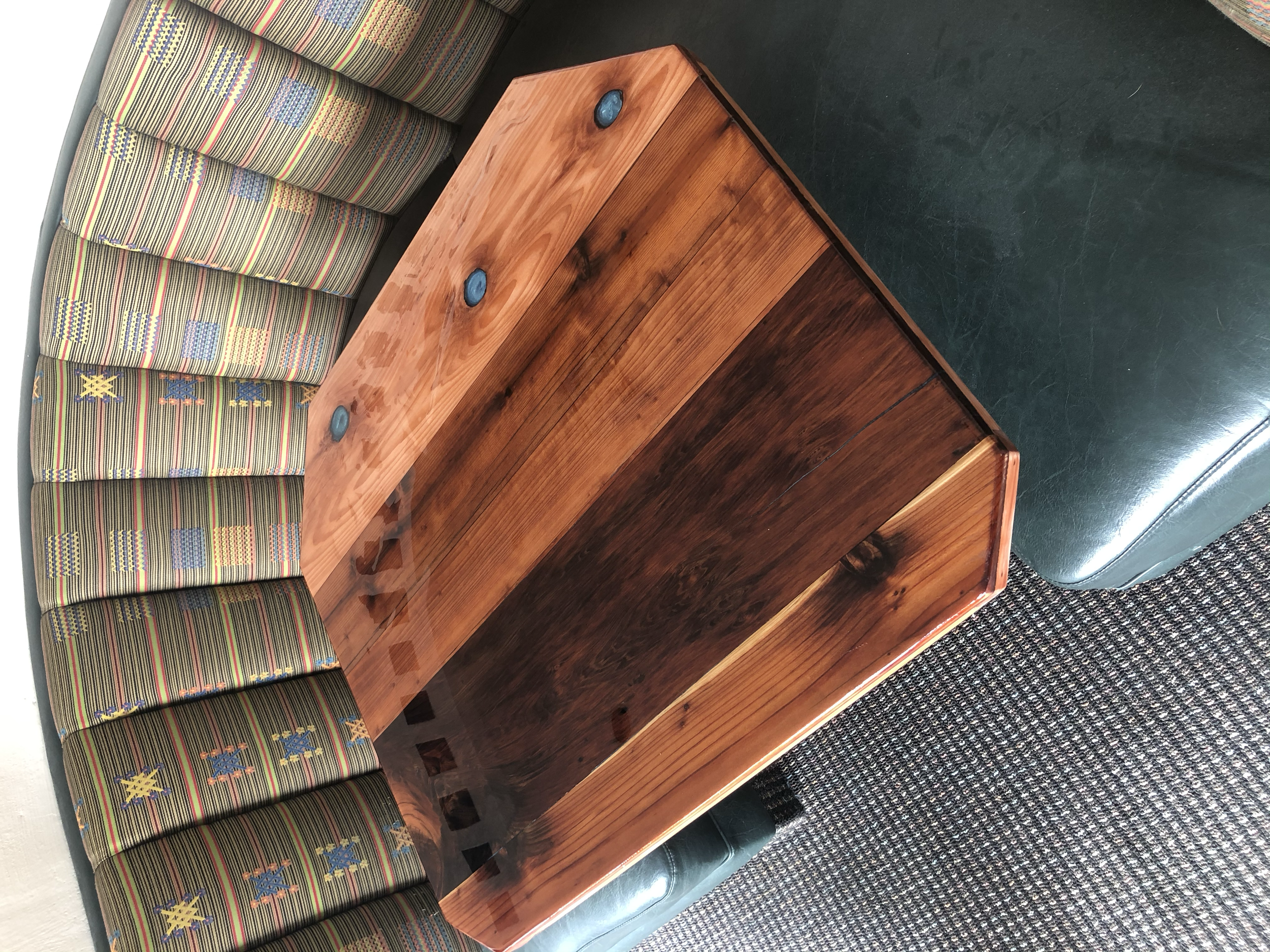 A wooden table with a curved edge, placed next to a patterned upholstered sofa and a green leather chair.