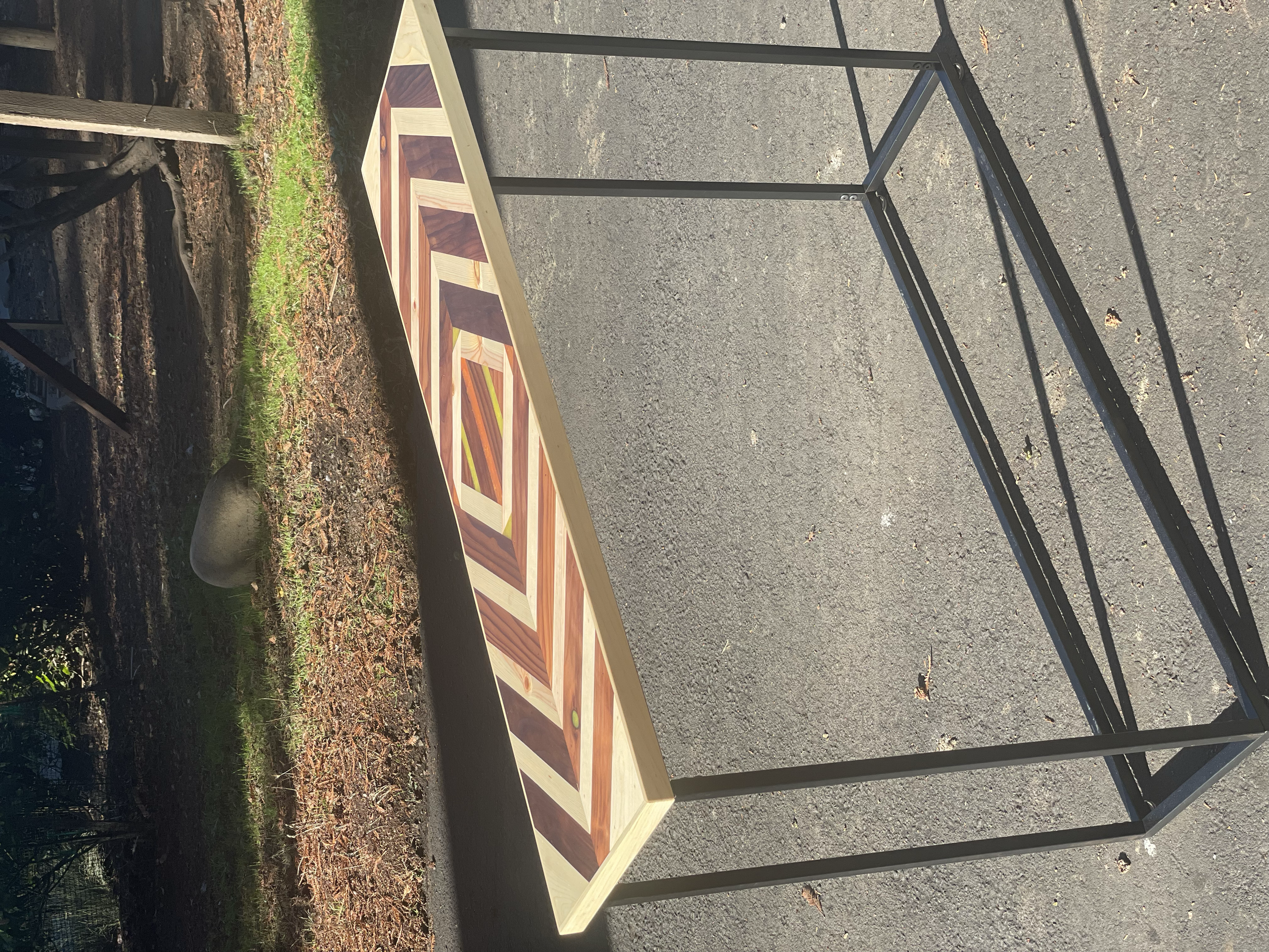 A partially assembled table with a colorful geometric patterned wooden top in an outdoor setting.