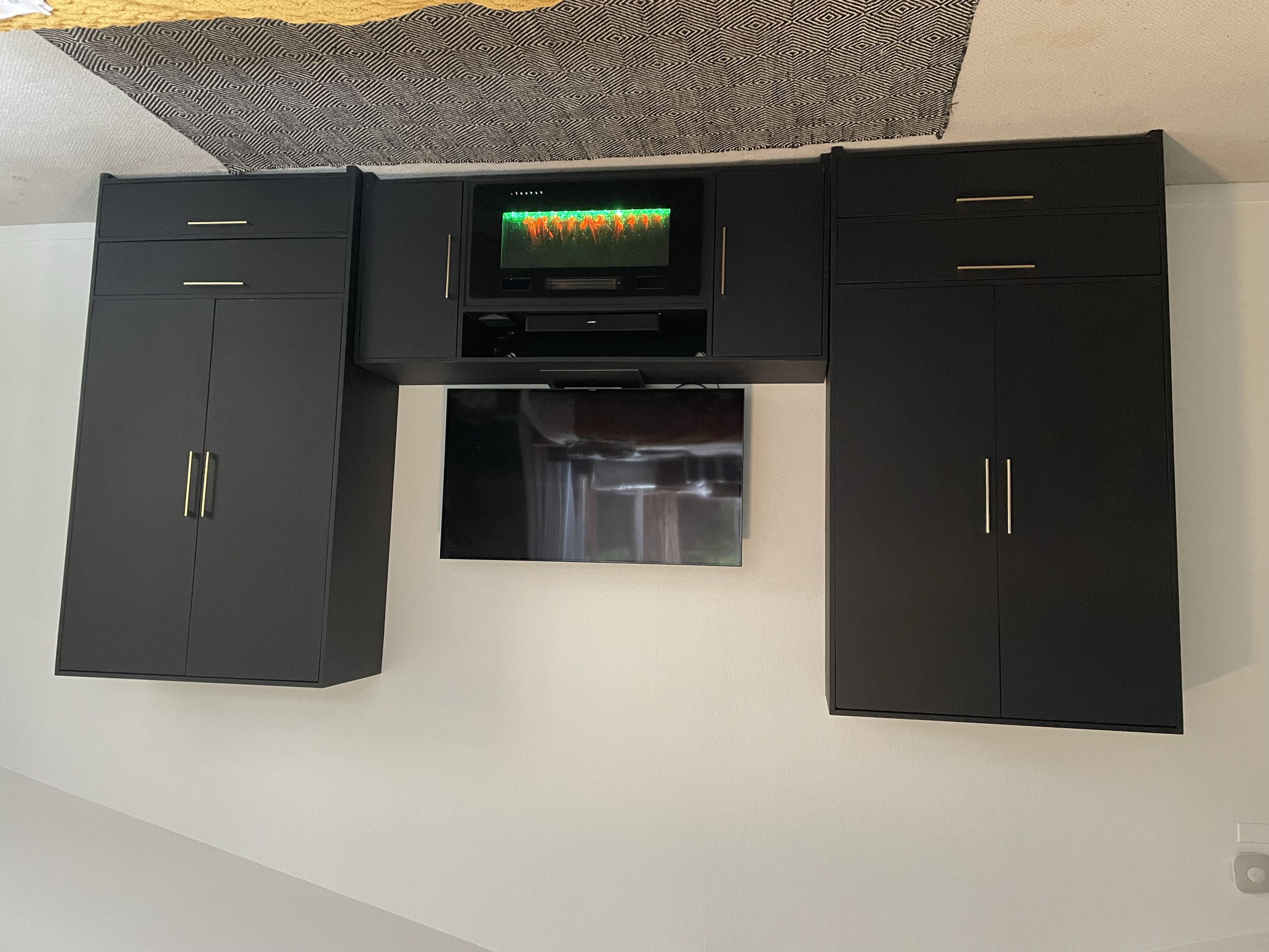 Black entertainment unit with a flat-screen TV, a small black microwave oven on top, and a decorative lighted display inside a glass front on the microwave.