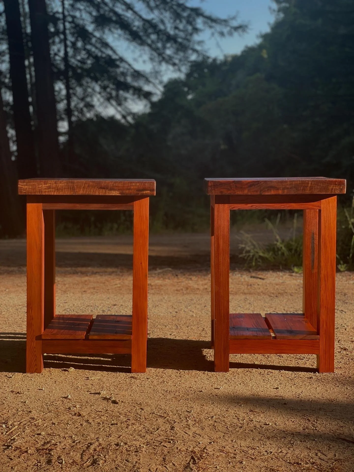 Two wooden stools placed on sandy ground outdoors with trees and sky in the background.