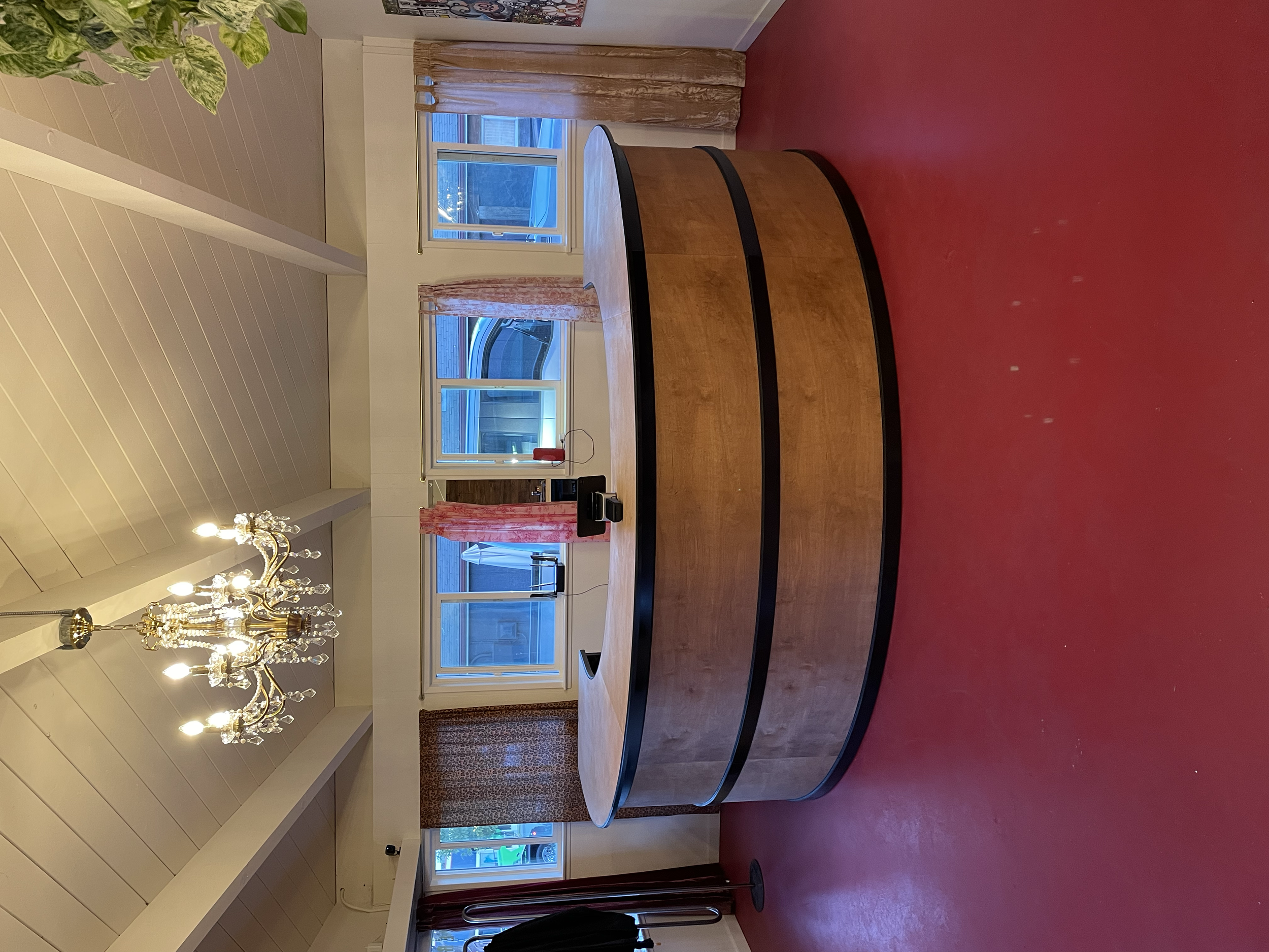 A dining room with a round wooden table, a chandelier hanging from the ceiling, and windows with pink curtains.