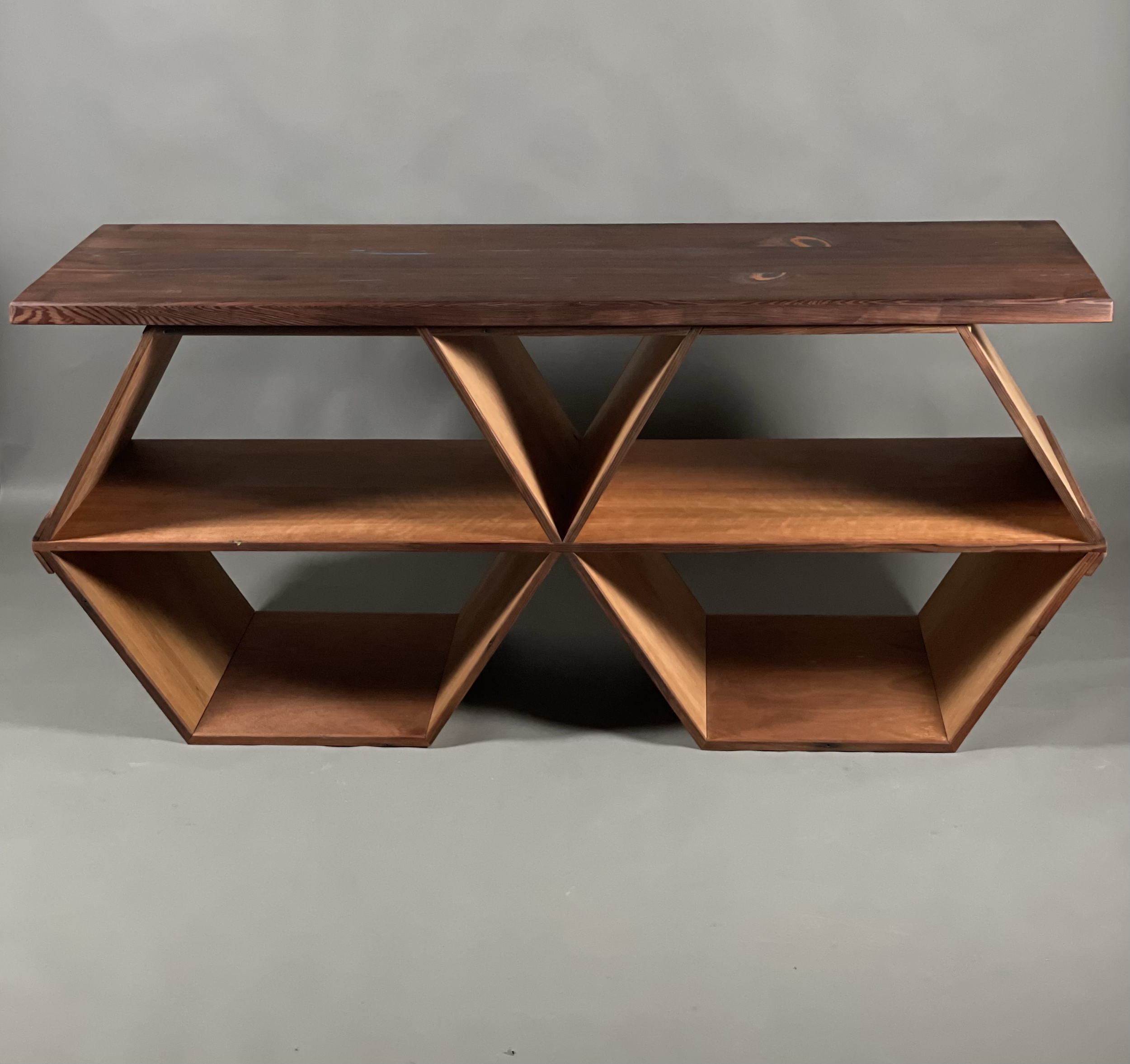 Wooden modern geometric shelving unit with two tiers and hexagonal compartments against a gray background.