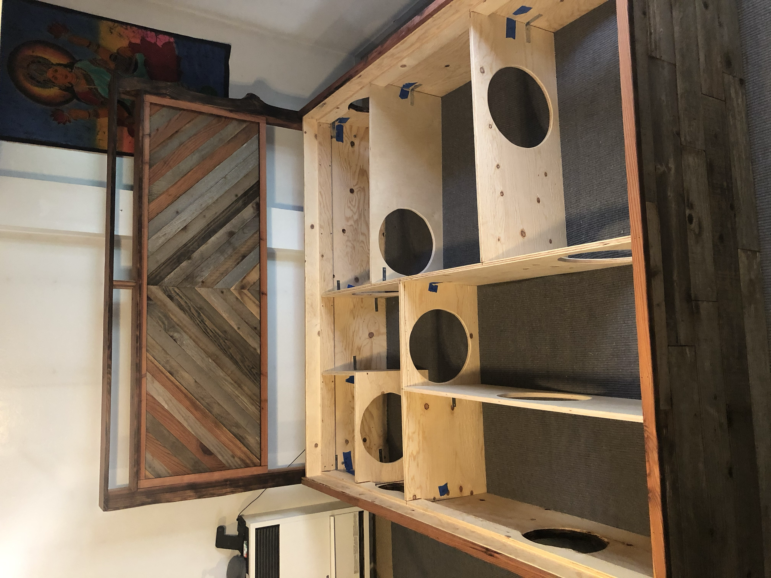 Unfinished wooden speaker box frame on a table with a wooden wall art piece in the background.