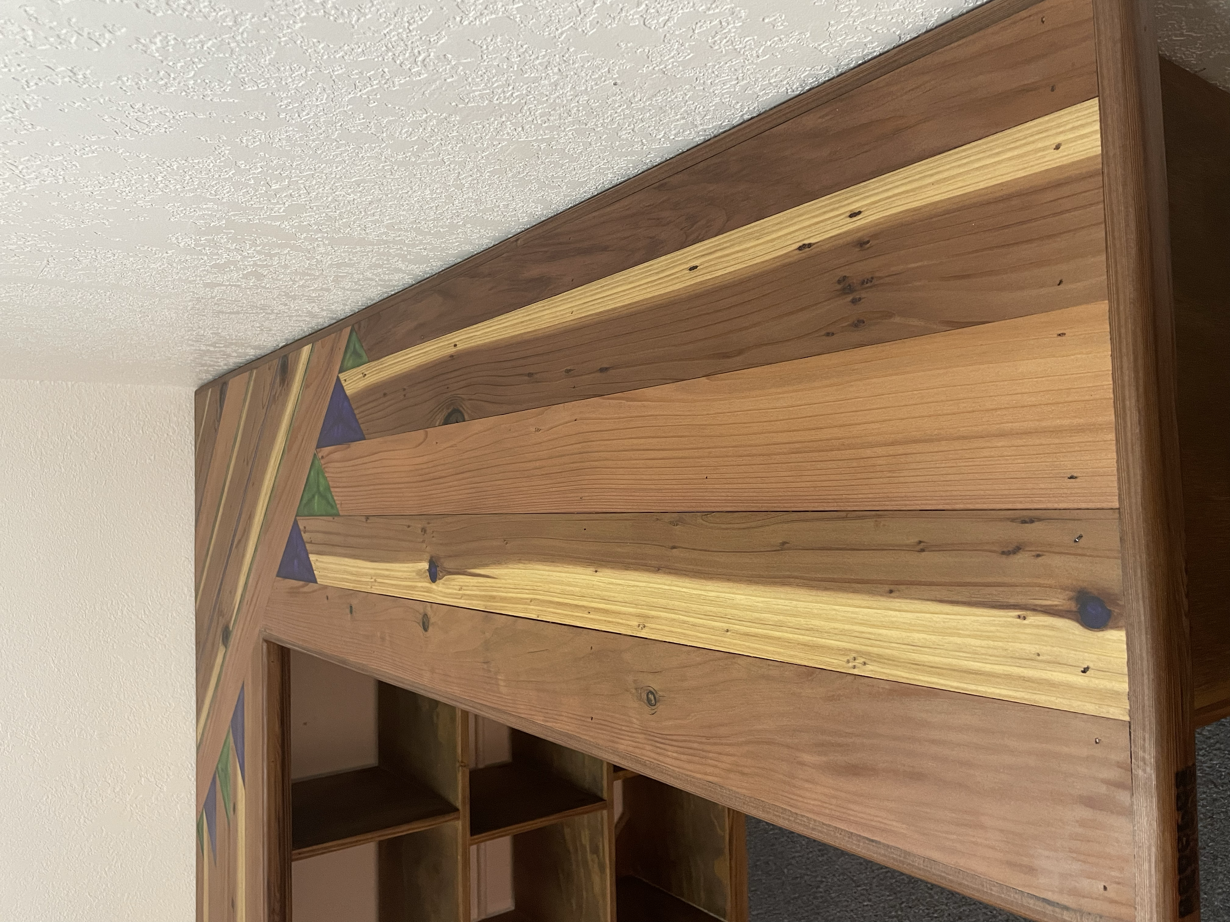 Close-up of a wooden desk with a colorful geometric design on the edge, featuring triangles in green, blue, and orange, with some compartments below.