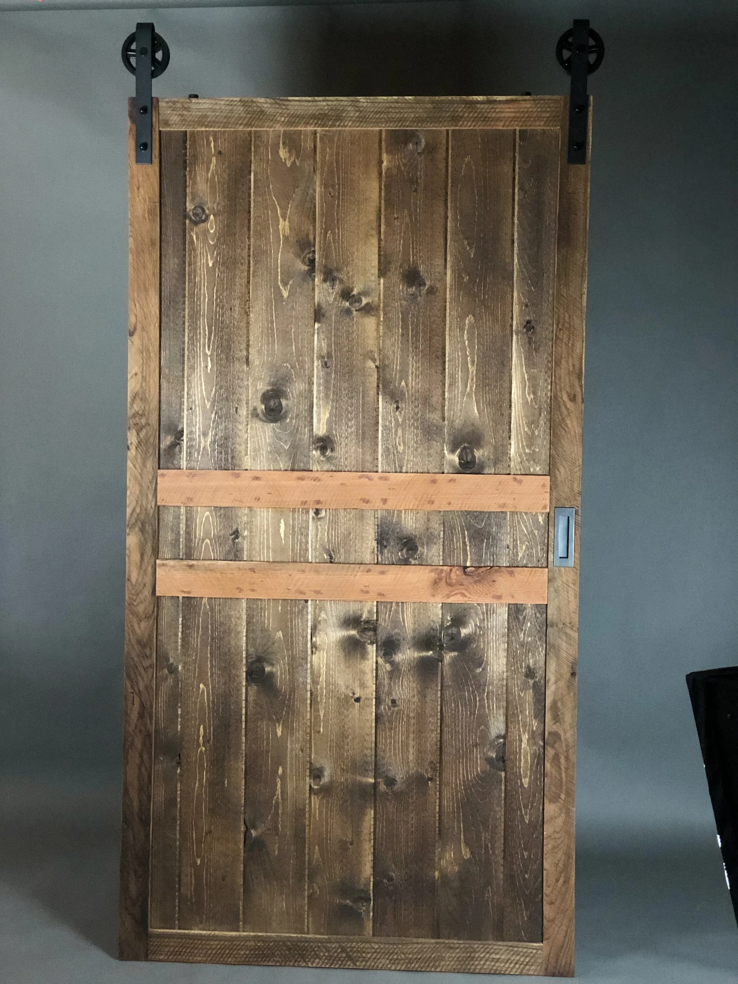 A wooden sliding barn door on black metal hardware attached to a gray wall.