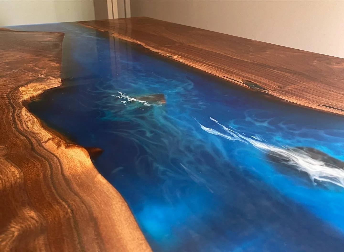 A wooden table with a natural edge, featuring a resin river design in blue and black, simulating flowing water.