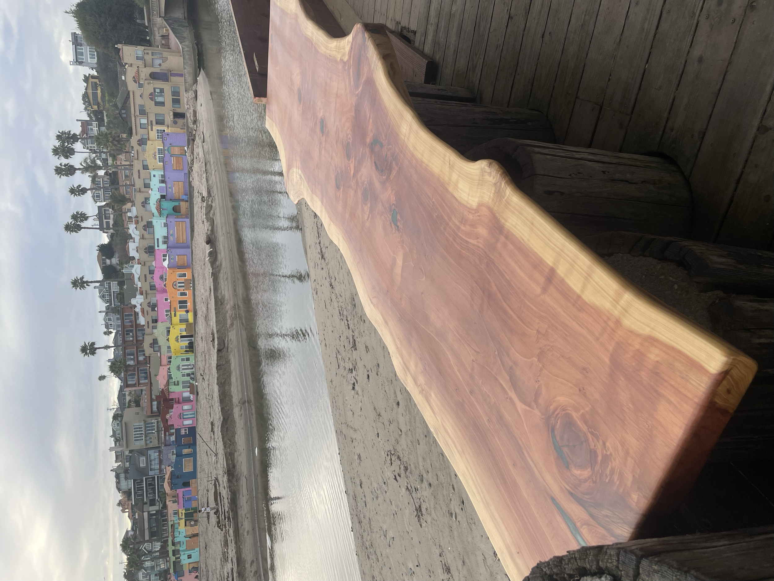 A wooden bench on a boardwalk overlooking colorful houses along a waterway, under an overcast sky.