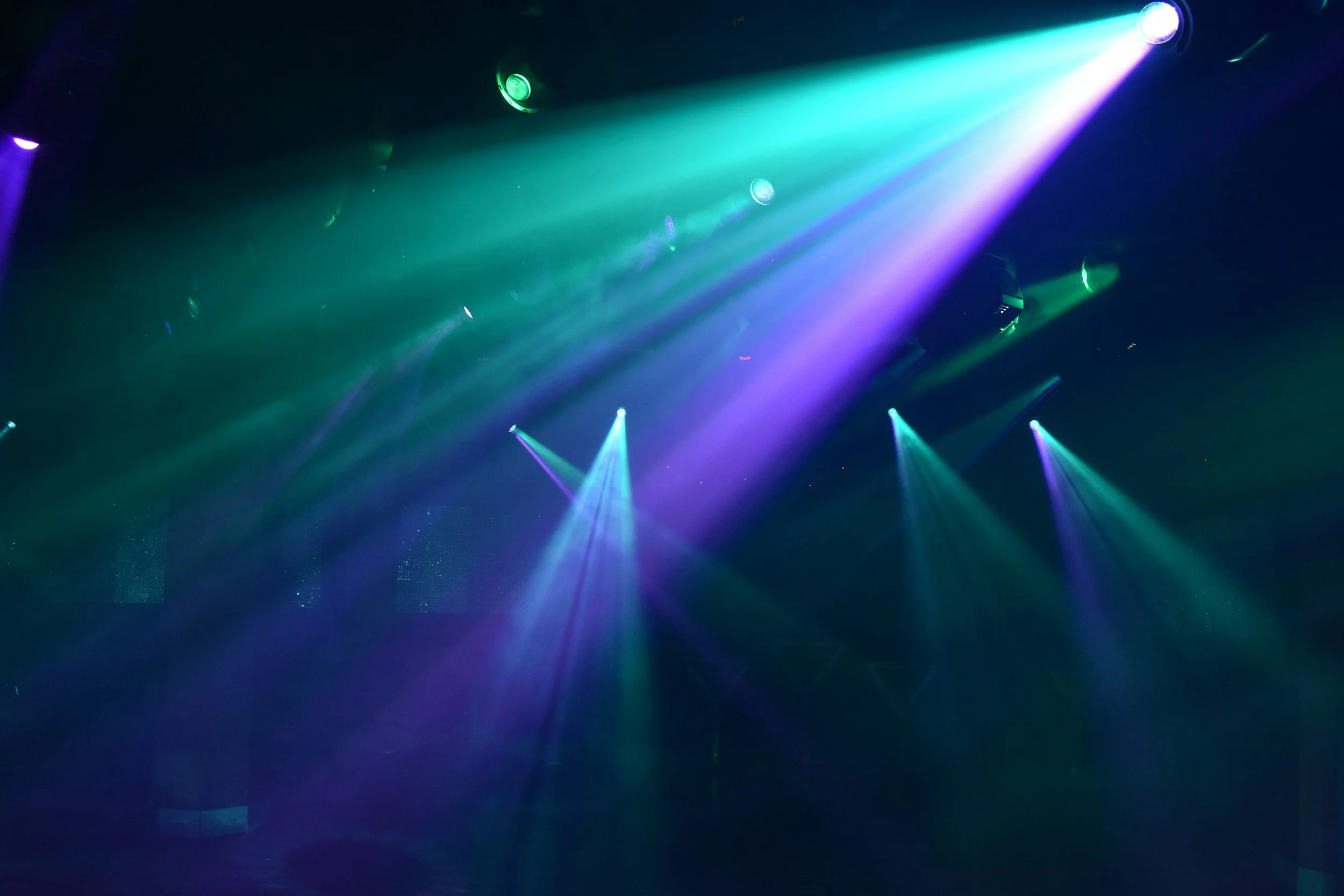 Luces de escenario de discoteca en tonos verdes, azules y morados proyectadas en un ambiente oscuro.