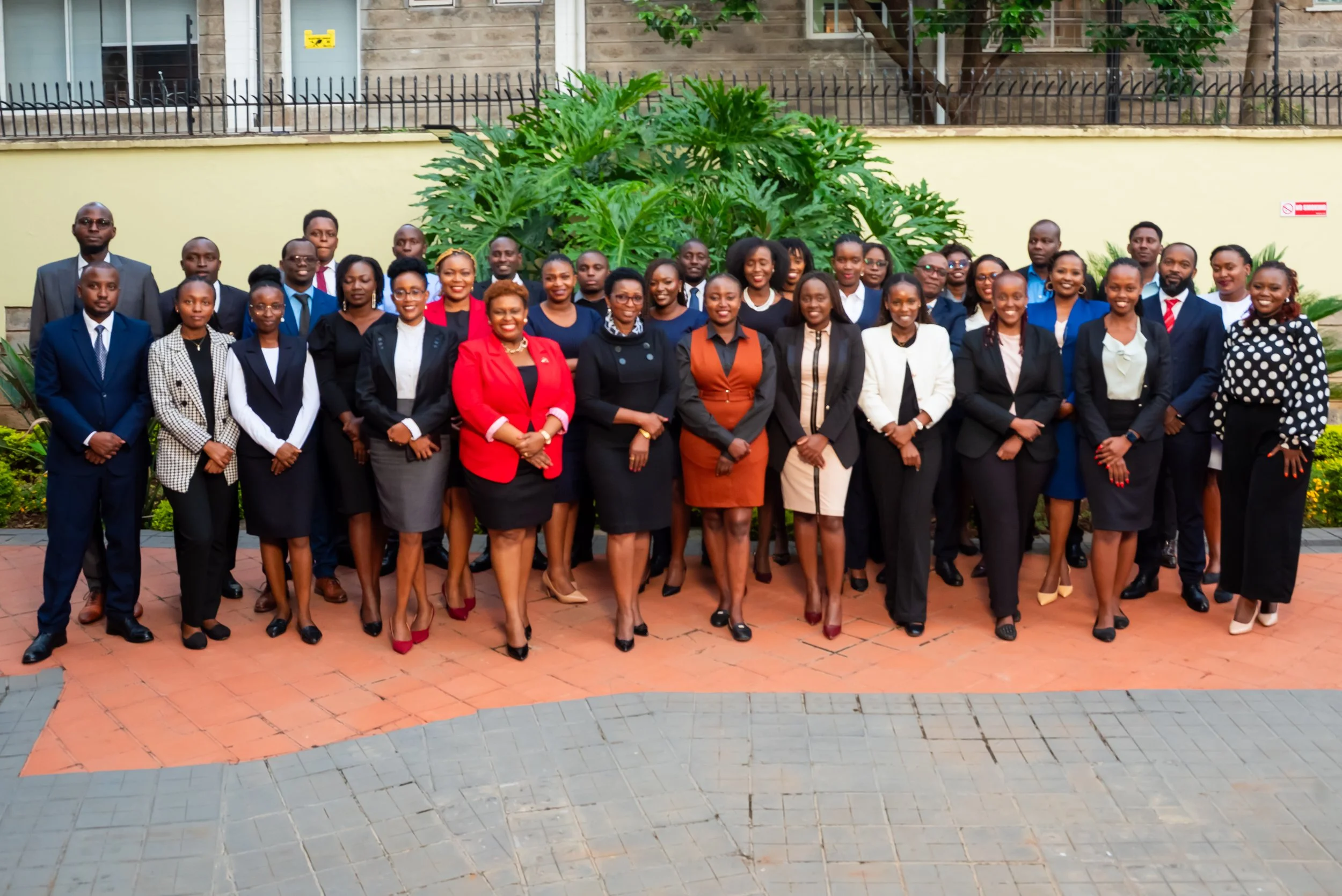 Viva's Team: A group of professionally dressed men and women standing outdoors, posing for a photo in front of green plants and a fence.