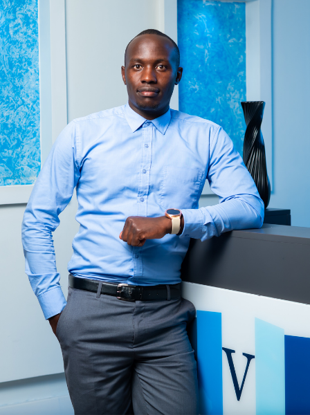 A man in a light blue dress shirt standing in a modern office, leaning on a reception desk with a large black decorative vase on it.
