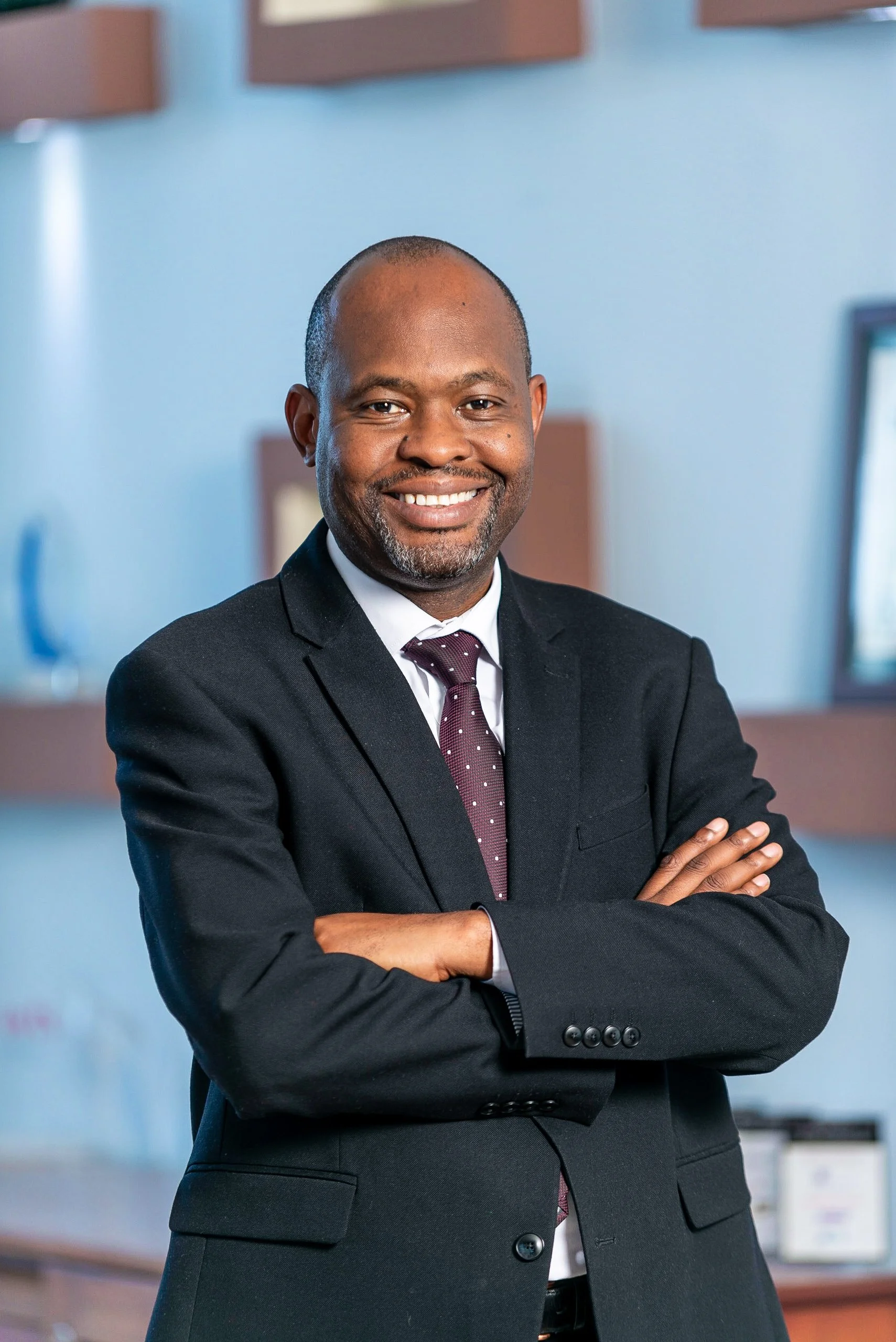 Edward Mwachinga, smiling with arms crossed, standing in an office environment.