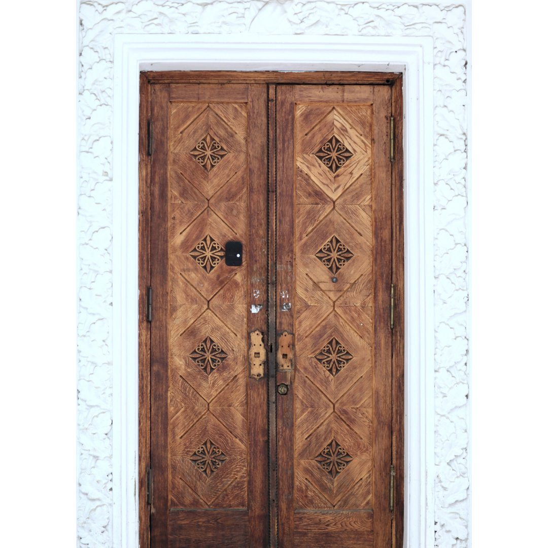 Wooden double door with cutout decorative designs and a black electronic lock, surrounded by ornate white moldings.