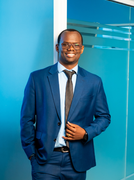 Smiling man in a blue suit and tie standing in front of a blue wall with glass panel.