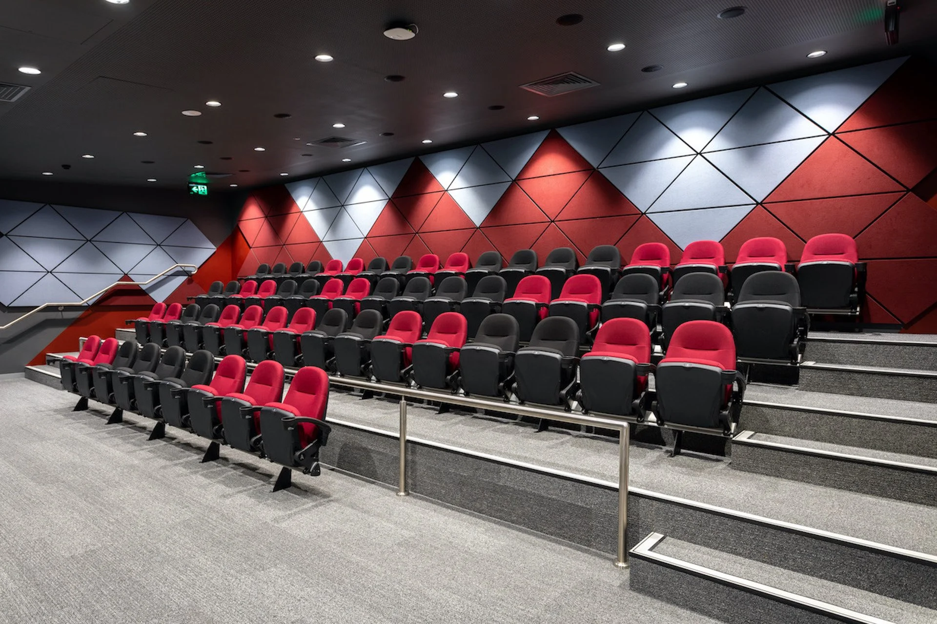 An empty movie theater with red and black seats on a sloped floor, and geometric red, gray, and white wall panels.