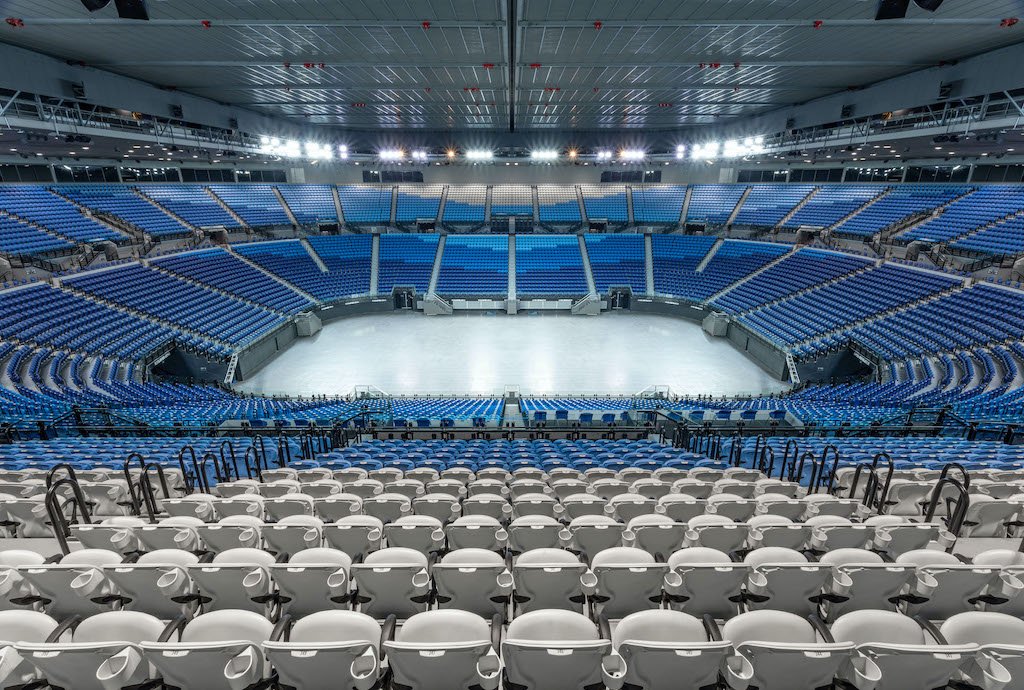 Empty indoor ice hockey arena with blue seating and a white ice rink.