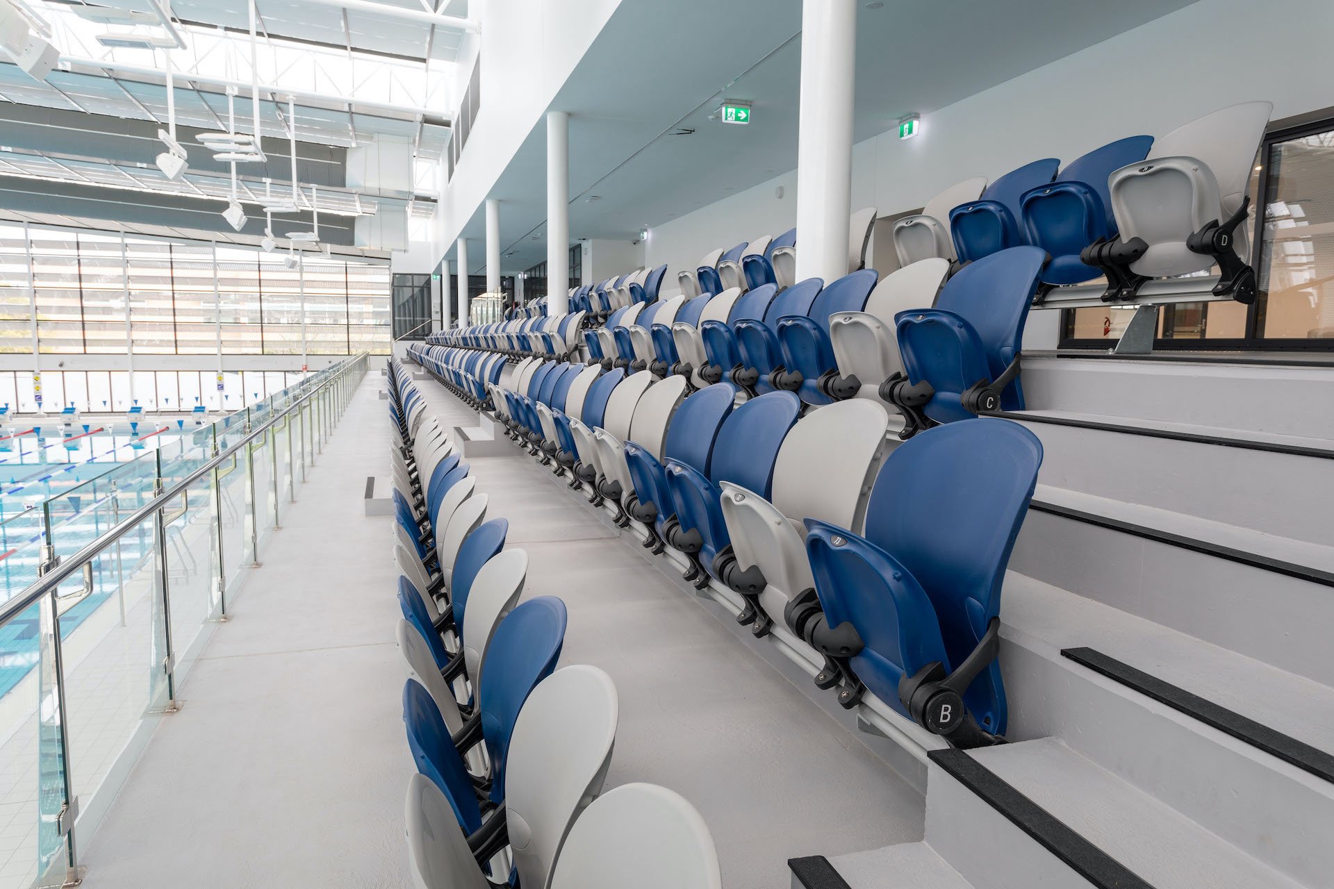 Empty indoor swimming pool with blue and white spectator seats on tiered stands beside the pool.