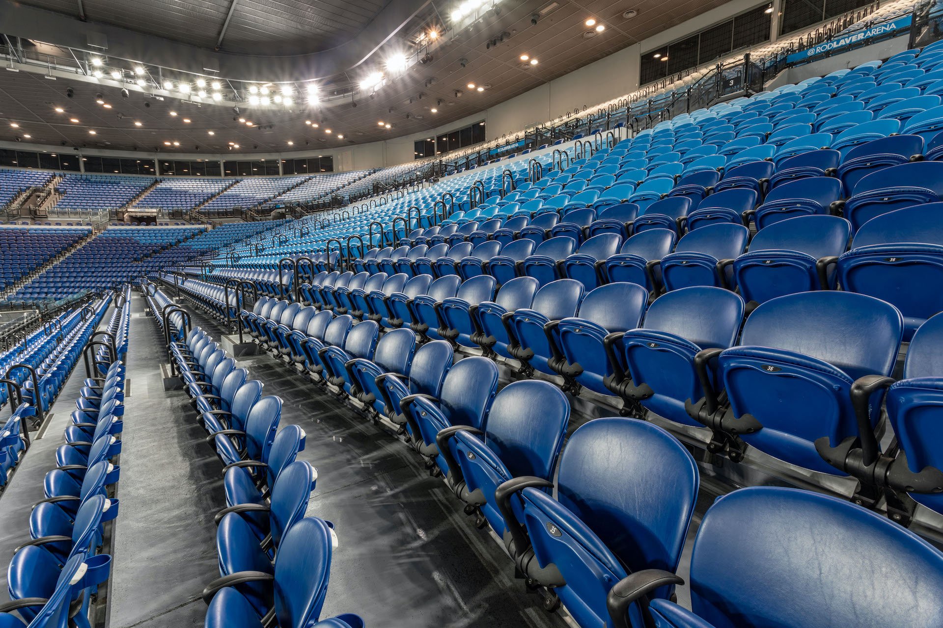 Empty blue seats in a large indoor sports arena with bright overhead lights.