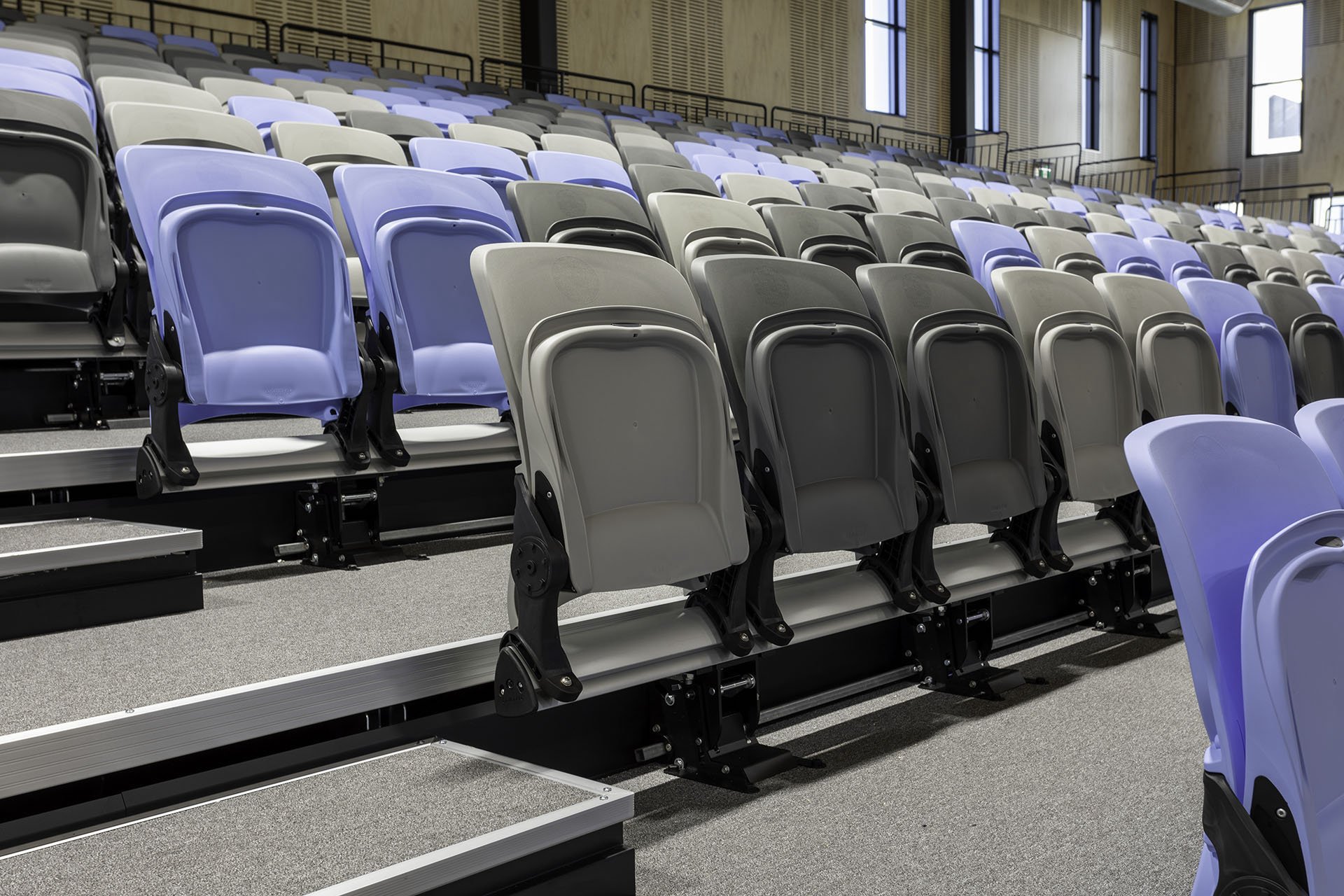 Empty auditorium with multi-colored tiered seating, including blue, gray, and black chairs.