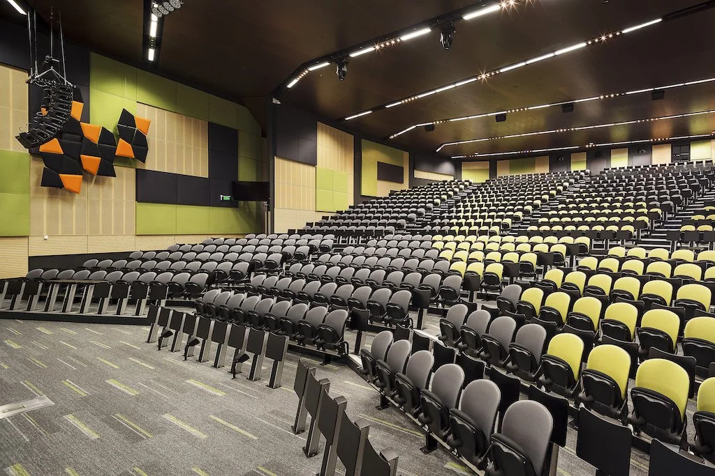 Empty auditorium with rows of black and yellow seats and a green and black soundproof wall.