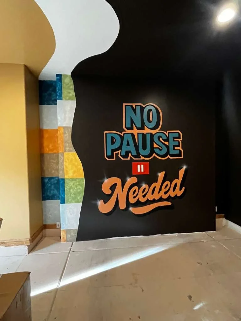 Decorative wall with colorful tile pattern on the left and a black wall on the right with a motivational quote 'No Pause Needed' written in large blue and orange lettering.