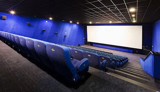 Sala cinematografica con poltrone blu e schermo grande sul muro.