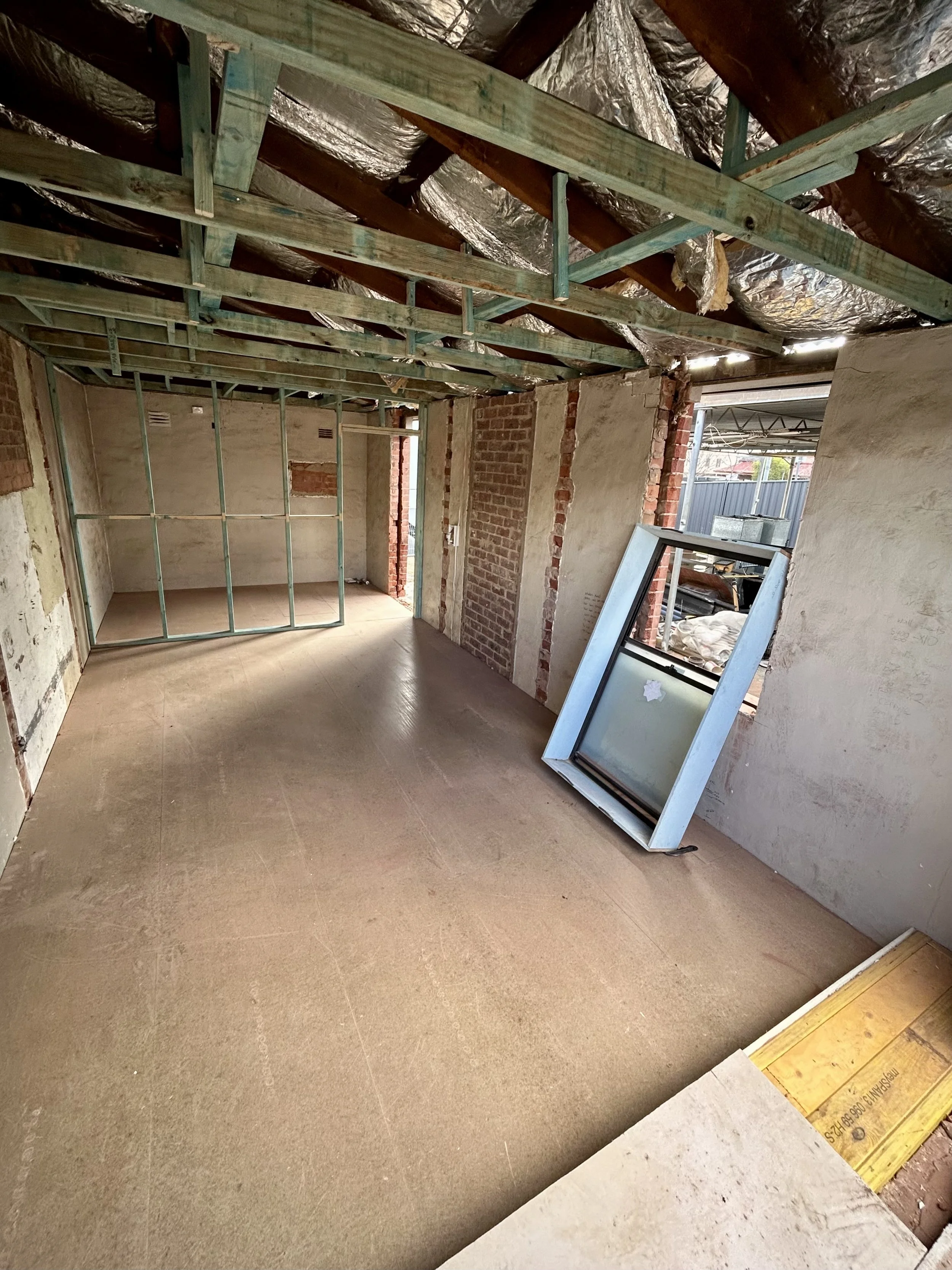 Interior view of a room under construction with framing, insulation, and a window frame leaning against the wall.